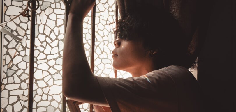 Un hombre reflexiona junto a una ventana que representa la atención a la salud mental masculina en Miami.